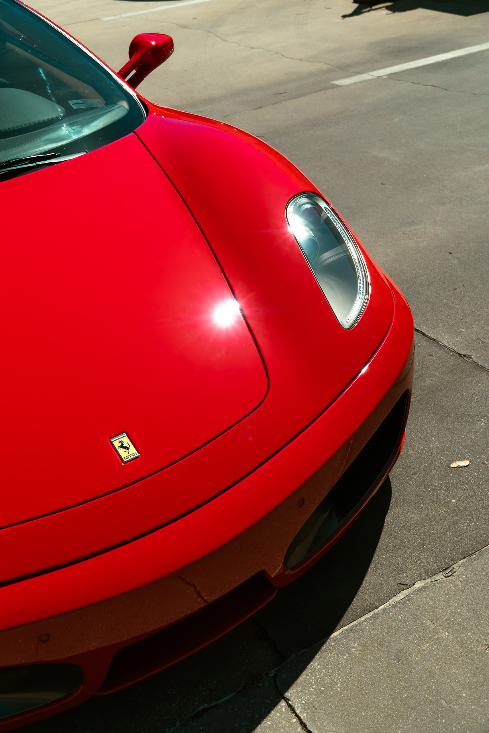 Overhead close-up of the red Ferrari F430 hood and headlight catching a bright sun glint
